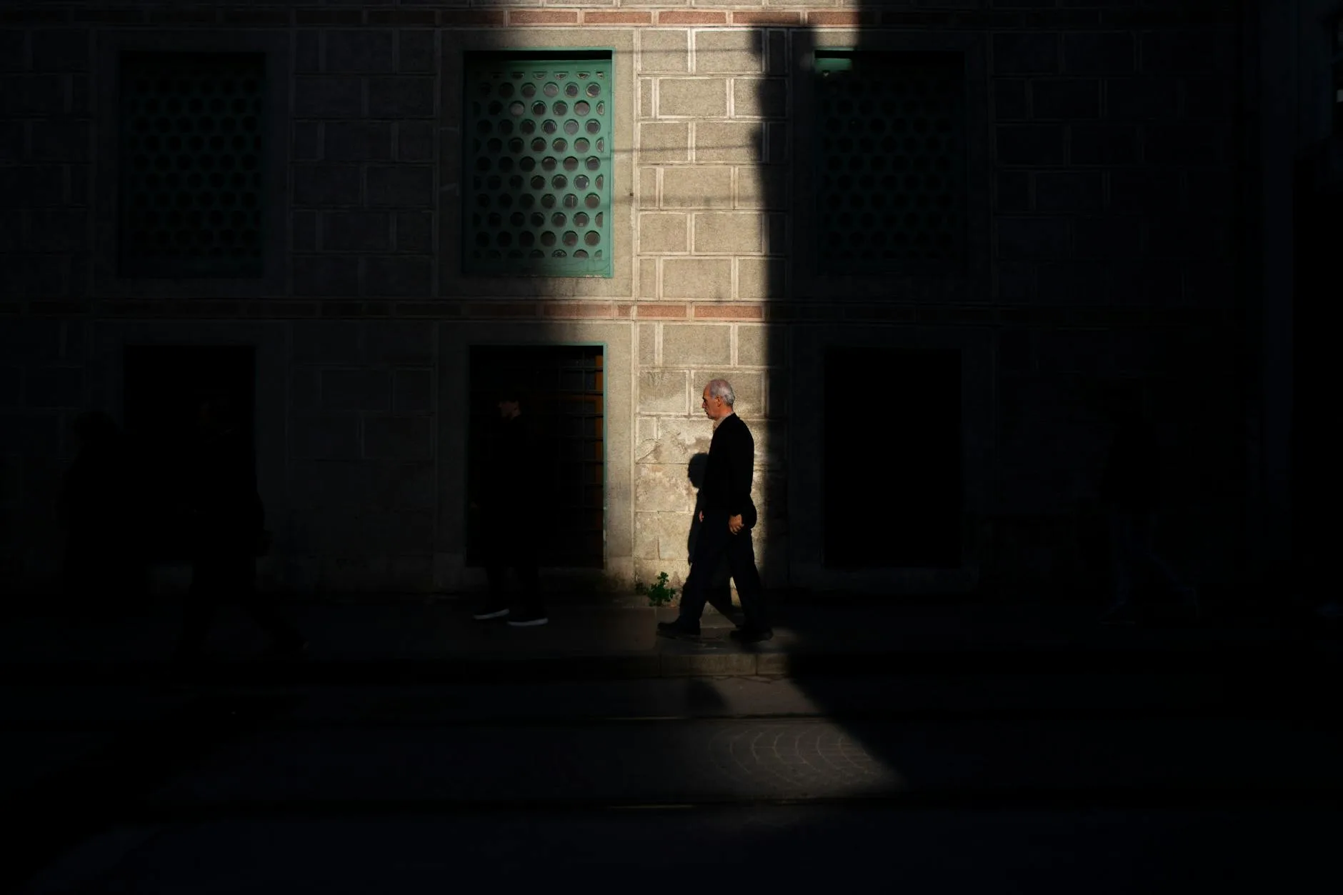 Mężczyzna idzie ciemną ulicą przy ceglanej ścianie, w ostrym świetle