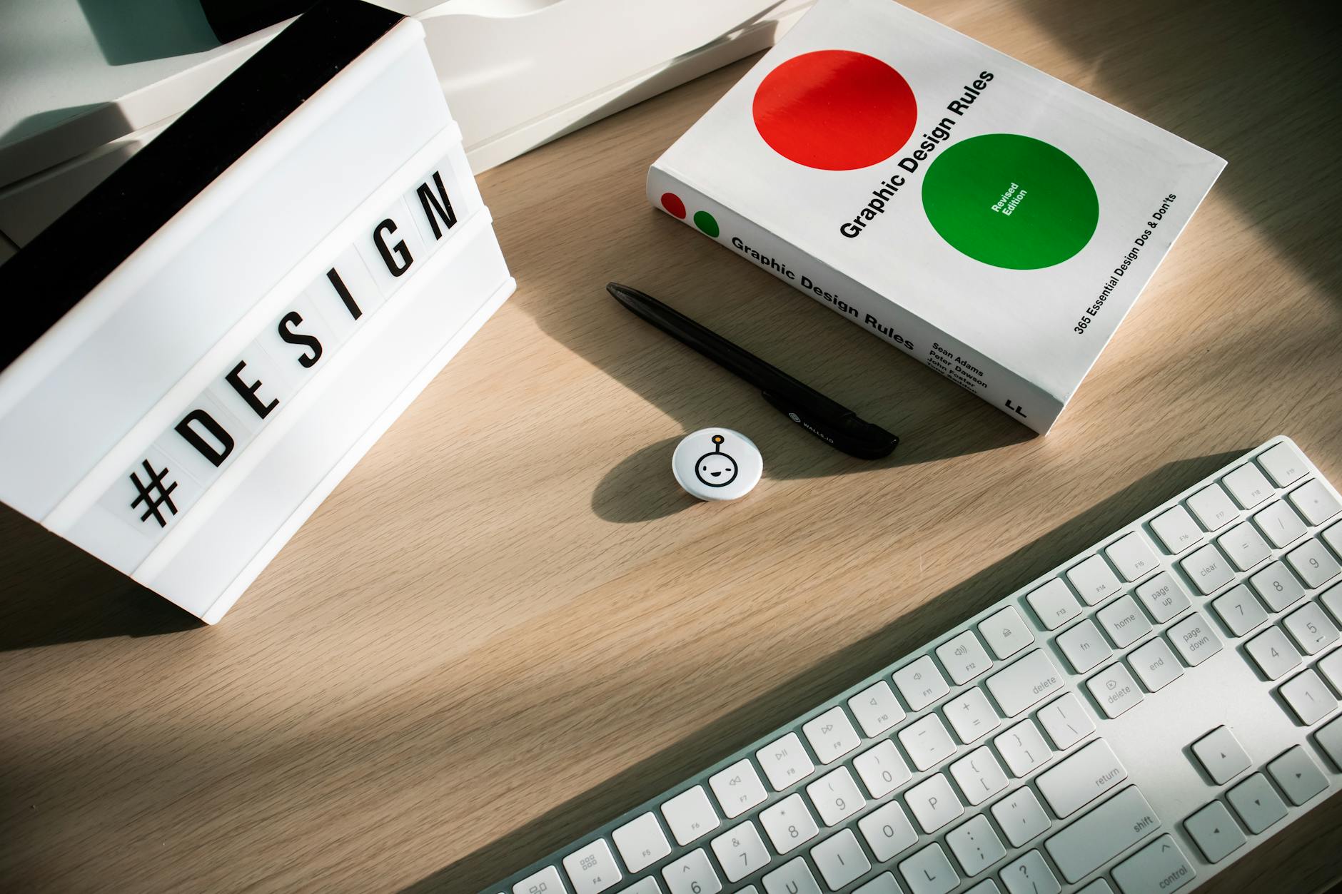 Biurko grafika z książką o designie, klawiaturą i świecącym hashtagiem