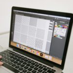 Dłoń przy laptopie z wyświetlonym projektem graficznym dla początkujących