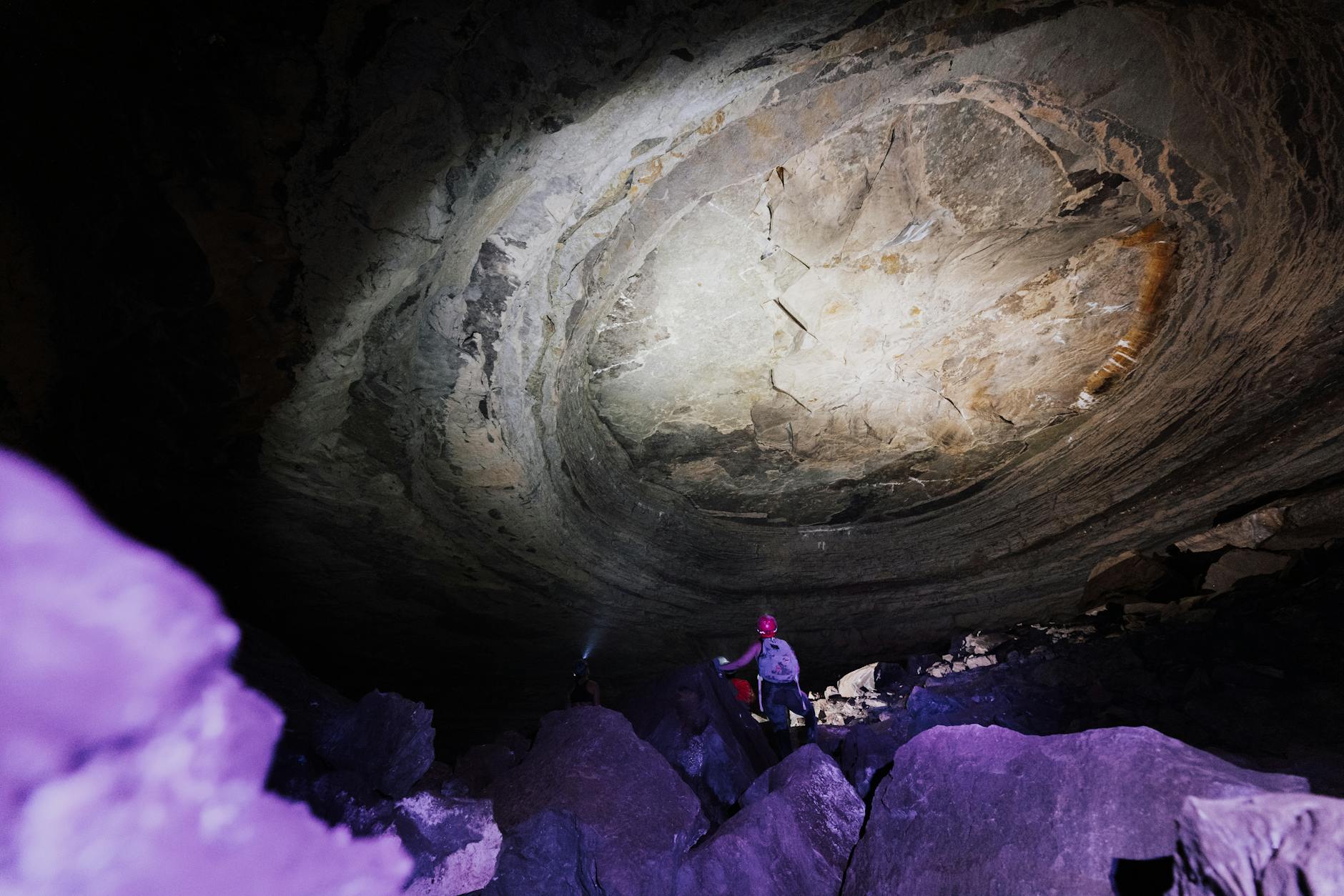 Grupa początkujących speleologów schodzi głębiej do oświetlonej jaskini