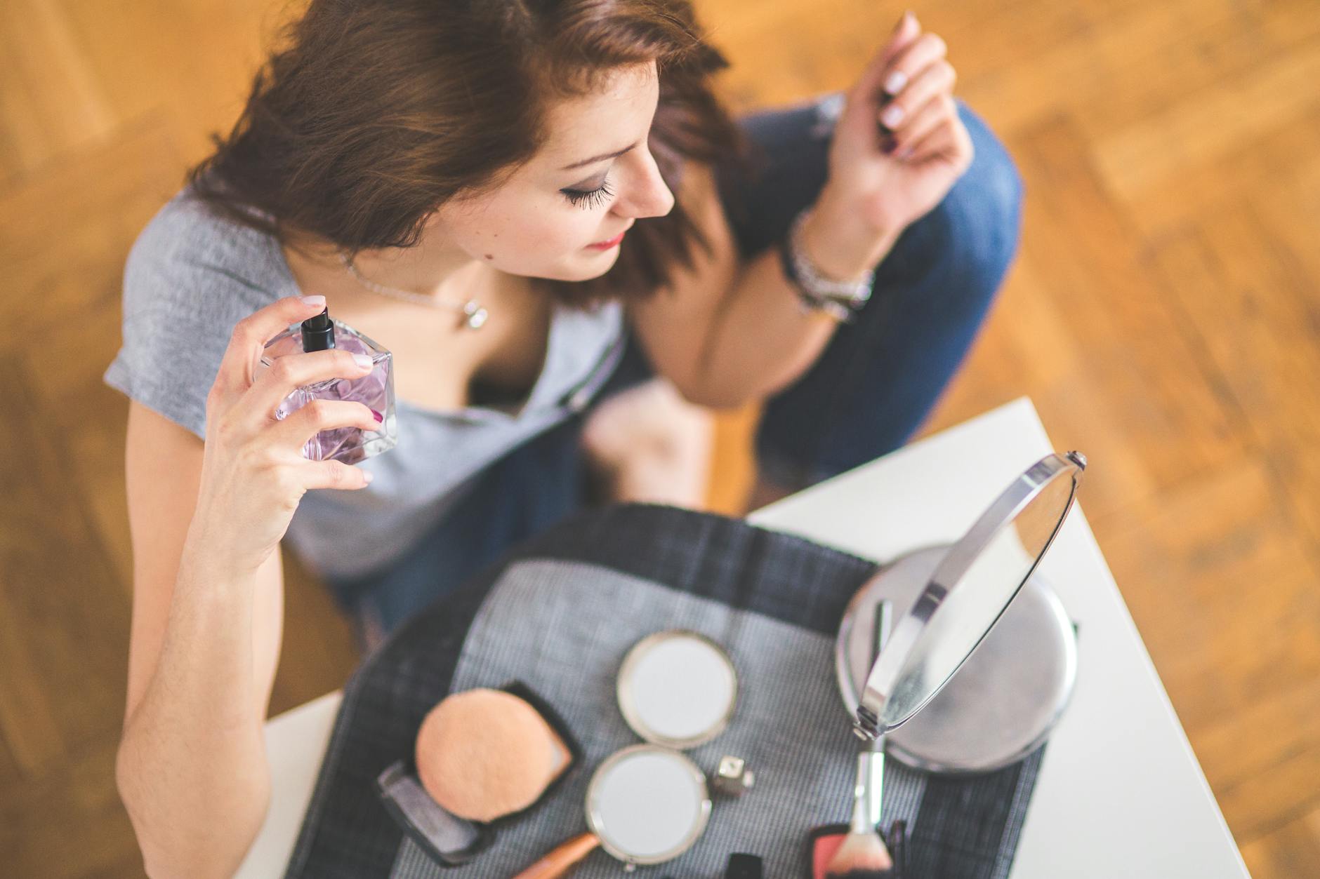 Młoda kobieta nakłada perfumy przy toaletce z kosmetykami