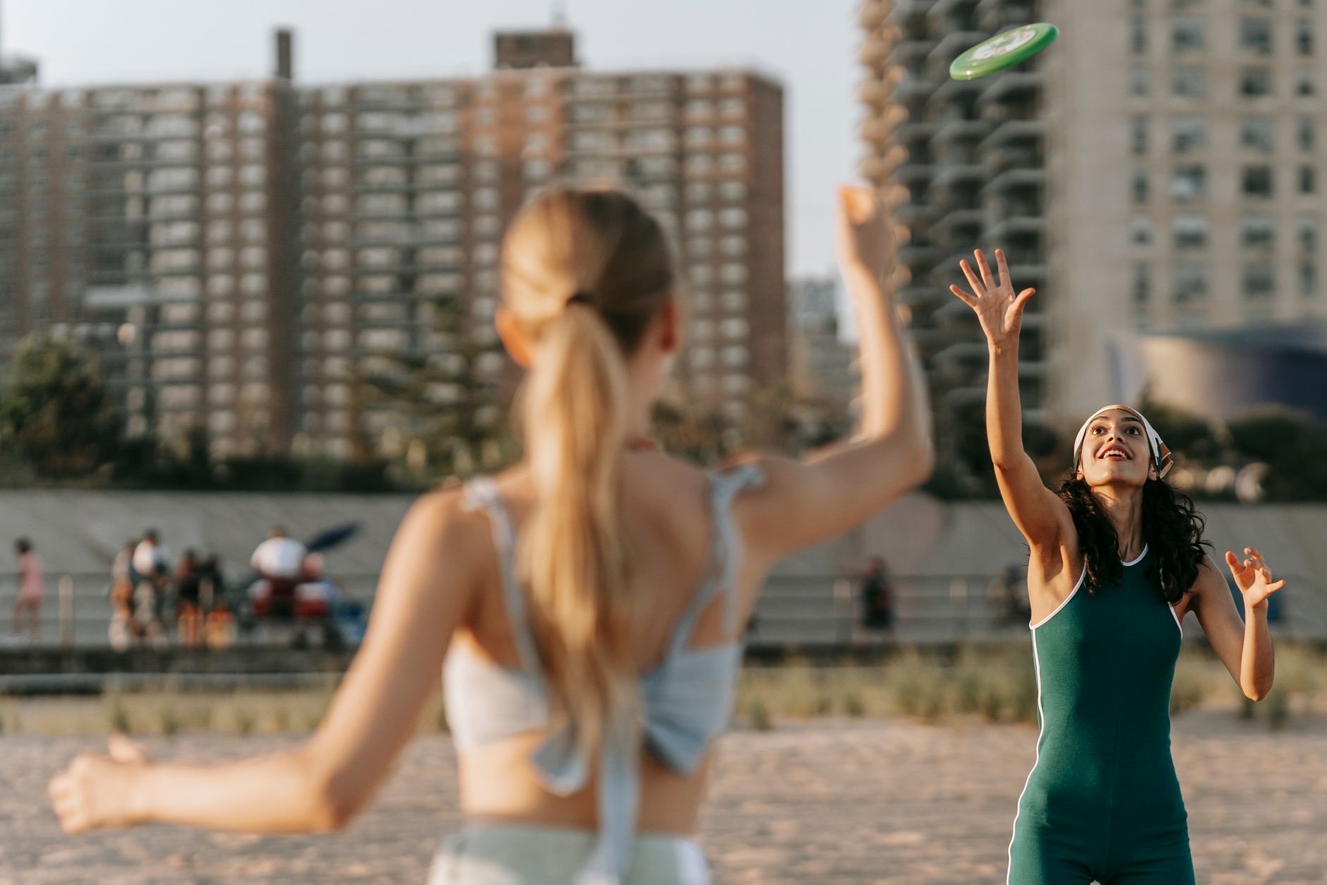 Jak zacząć trening frisbee w mieście – poradnik dla amatorów sportów niszowych Dwie kobiety rzucają frisbee na plaży z widokiem na miasto
