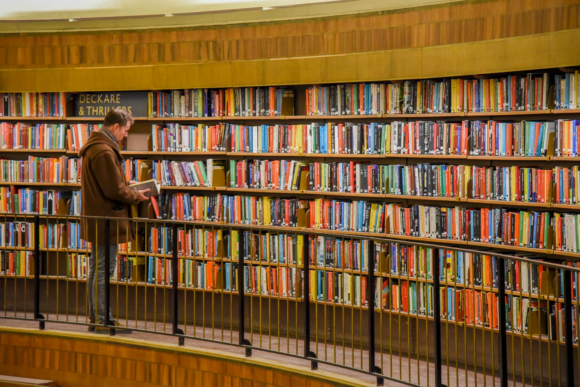 Mężczyzna wybiera książkę z kolorowej półki w miejskiej bibliotece